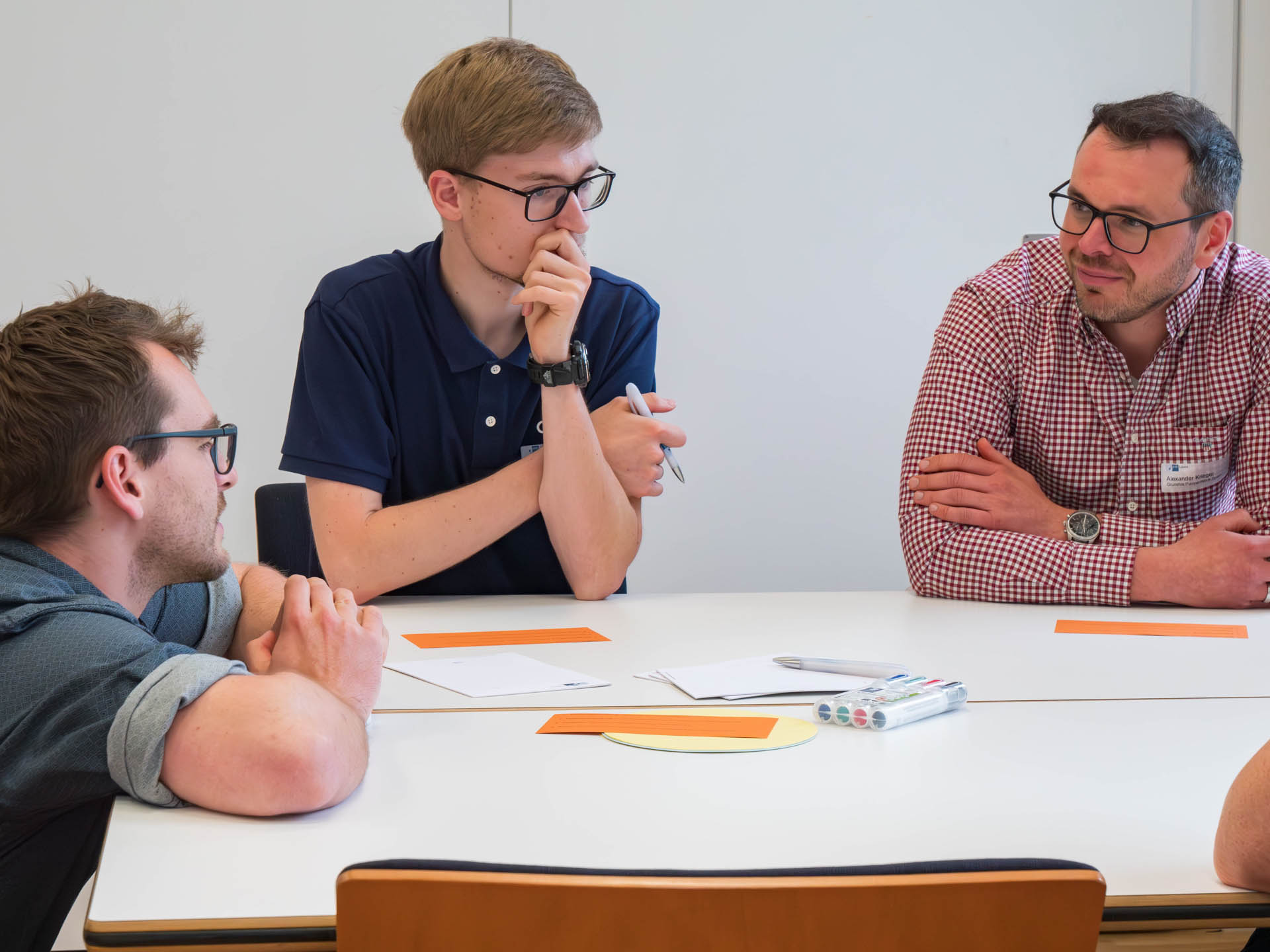 Drei Männer sprechen an einem Tisch mit Zetteln und Stiften